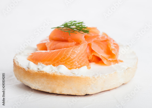 Fresh healthy bagel sandwich with salmon, ricotta and dill on light kitchen table background. Healthy diet food.