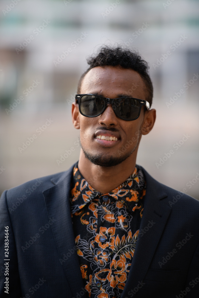 Face of happy young African businessman with sunglasses smiling outdoors
