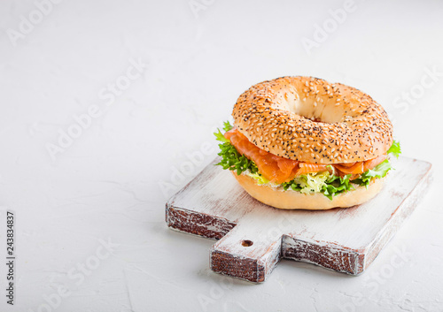 Fresh healthy bagel sandwich with salmon, ricotta and lettuce on vintage chopping board on stone kitchen table background. Healthy diet food. Space for text