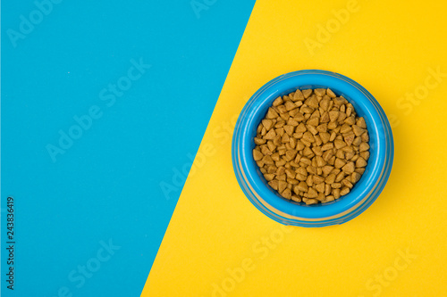 Blue round feeding bowl with pet dried food on a blue and yellow background with space for copy