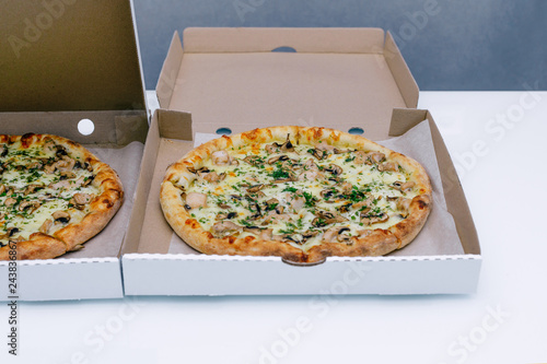 Two pizzas in a cardboard box on a light background. Top view. Pizza delivery. Pizza menu. Pizza on the kitchen table.