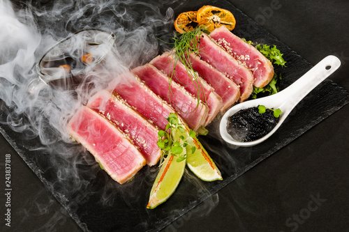 Sliced tuna steak with lime and sesame in puffs of white smoke.