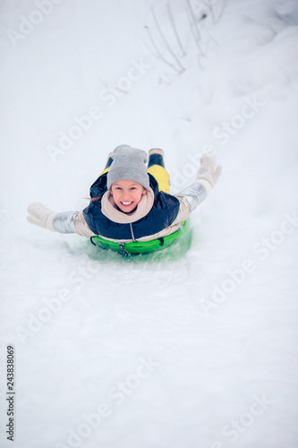 Adorable little happy girl sledding in winter snowy day.