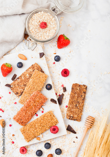 Organic cereal granola bar with berries on marble board with honey spoon and jar of oats and linen towel on marble background. Raw wheat bundle photo