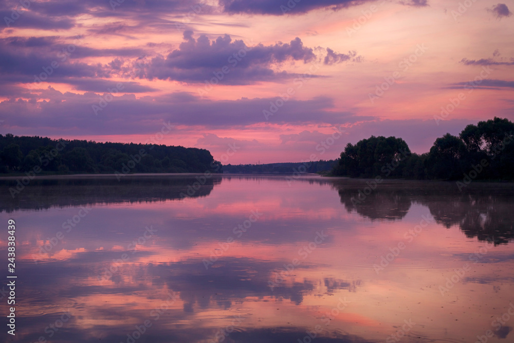 Beautiful pink dawn. Clouds are reflected in the water of the lake in the early morning.