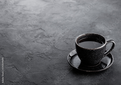 Black coffee cup with saucer on black stone kitchen table background. Space for text