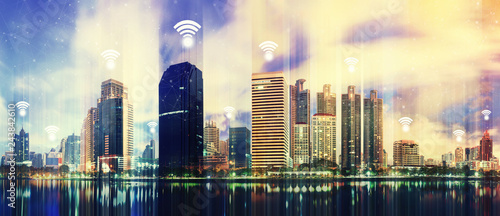 Modern building in city with wifi connection icons in the sky. Wireless network connection concept. © tawanlubfah