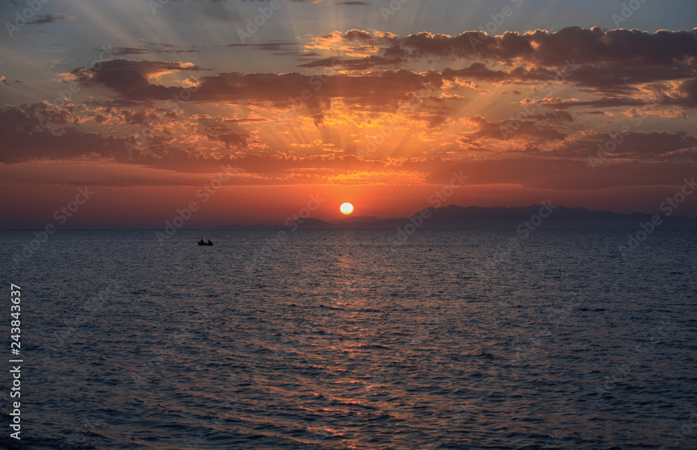 Fototapeta premium Beautiful view of the sea at sunset, the sun on the horizon and the rays in the clouds
