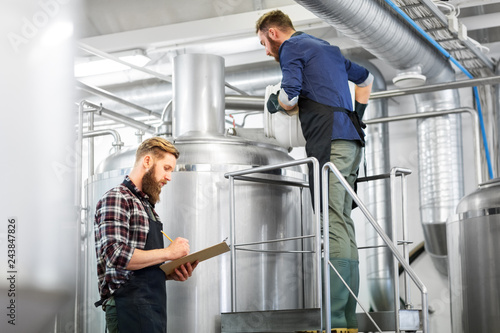 manufacture, business and people concept - men with clipboard and malt working at brewery or beer plant kettle