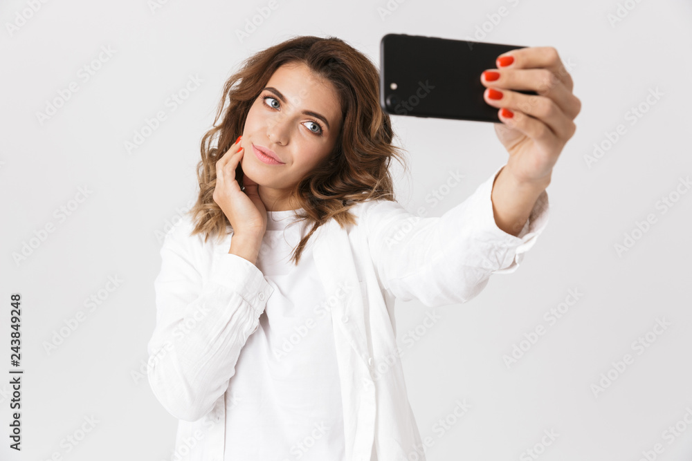 Portrait of happy woman in casual clothes taking selfie photo on cell phone, while standing isolated over white background Portrait of happy woman in casual clothes taking selfie photo on cell phone, while standing isolated over white background