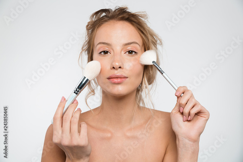 Woman posing isolated over white wall background holding makeup brushes.
