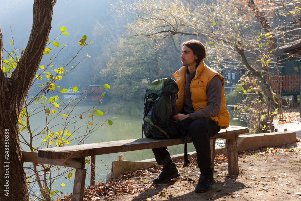 Fototapeta premium Man taking a rest on the bench by the lake while hiking in nature.