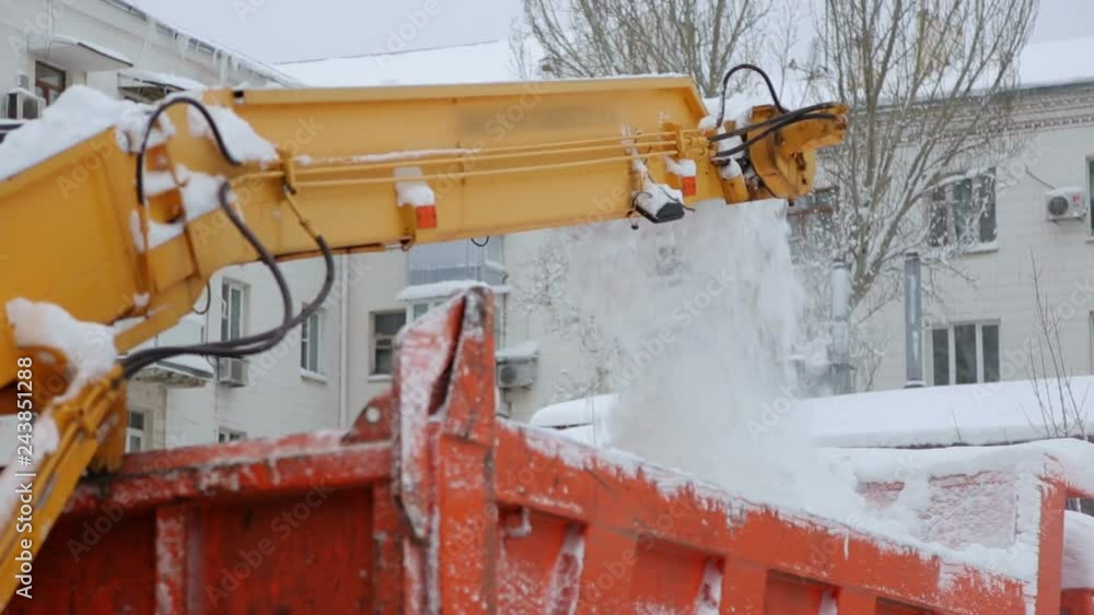 Close-up process of working snow plow. Snow plow loads snow into the truck body. City workers clearing snow from the roads after heavy winter snowfalls. Close-up process of working snow plow. Snow plow loads snow into the truck body. City workers clearing snow from the roads after heavy winter snowfalls.