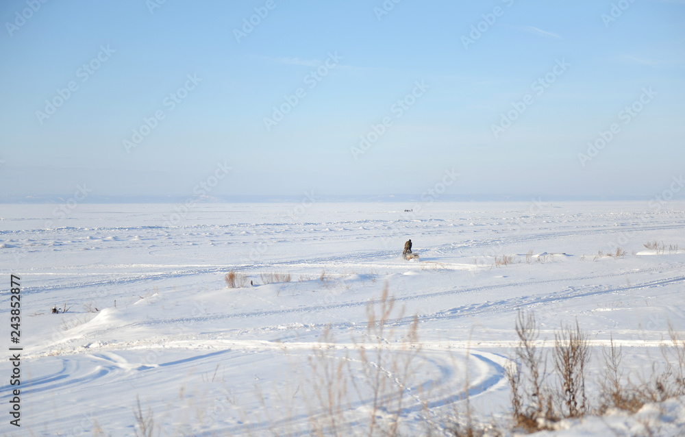 Winter snow landscape. Endless space of a frozen river. A single fisherman goes fishing Winter snow landscape. Endless space of a frozen river. A single fisherman goes fishing