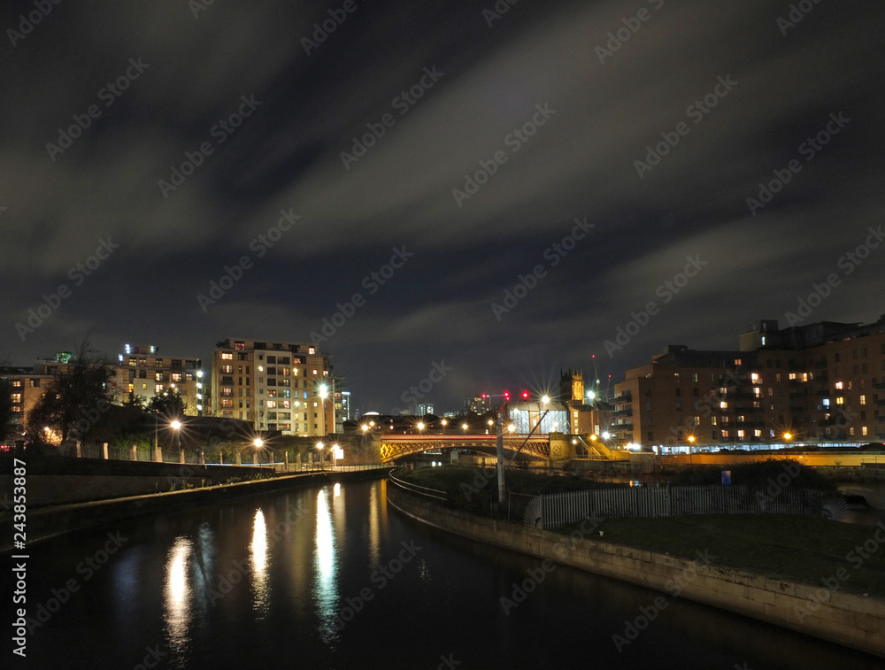 panoramic cityscape view of leeds at night from the river aire with crown point bridge and apartments reflected in the water and parish church illuminated behind modern developments