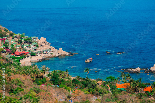 Tannot Bay on Koh Tao island. The rocks on the shore of a tropical forest with coconut trees. Bungalow on the beach. Cozy hotels. Blue water of the South China sea. Ship and boat in the Bay