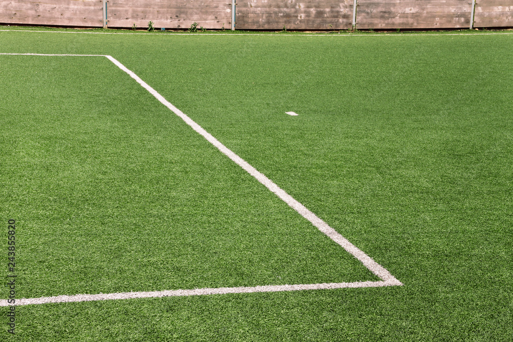 Part of sport soccer stadium and artificial turf football field. Detail, close up of green grass with white lines, goal line, corner line. Focus football field selected background, texture, wallpaper.