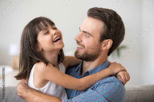 Happy dad holding cute cheerful kid daughter laughing enjoy good time together, loving father and smiling little girl hugging, caring daddy embracing funny child relaxing playing having fun concept