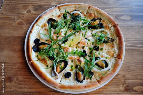 Seafood pizza with mussels, squid and shrimps, topped with olives, onion, herbs and lemon