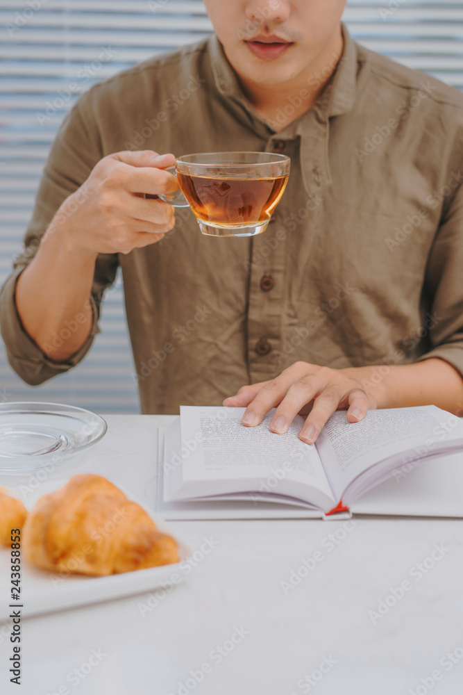 Man eating breakfast and reading book while sitting at a white table Man eating breakfast and reading book while sitting at a white table