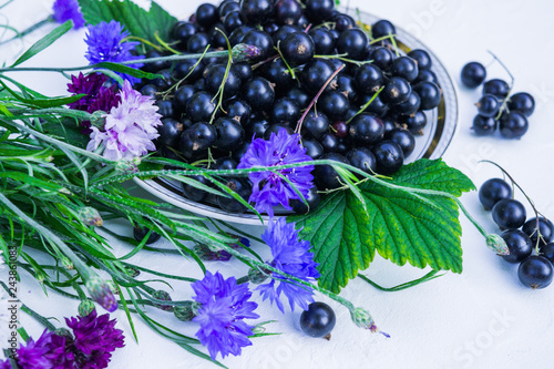 Fresh berries of black currant in a plate on a table together with cornflowers . For a diet and saturation with vitamins photo