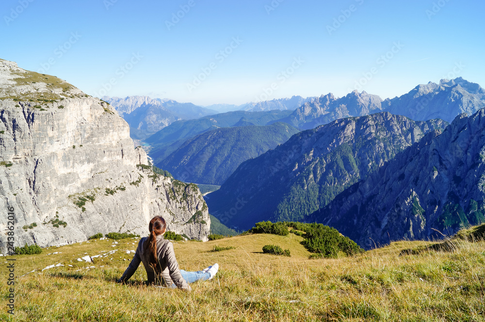 girl sits on the grass and admires the beautiful mountain view in the Alps
