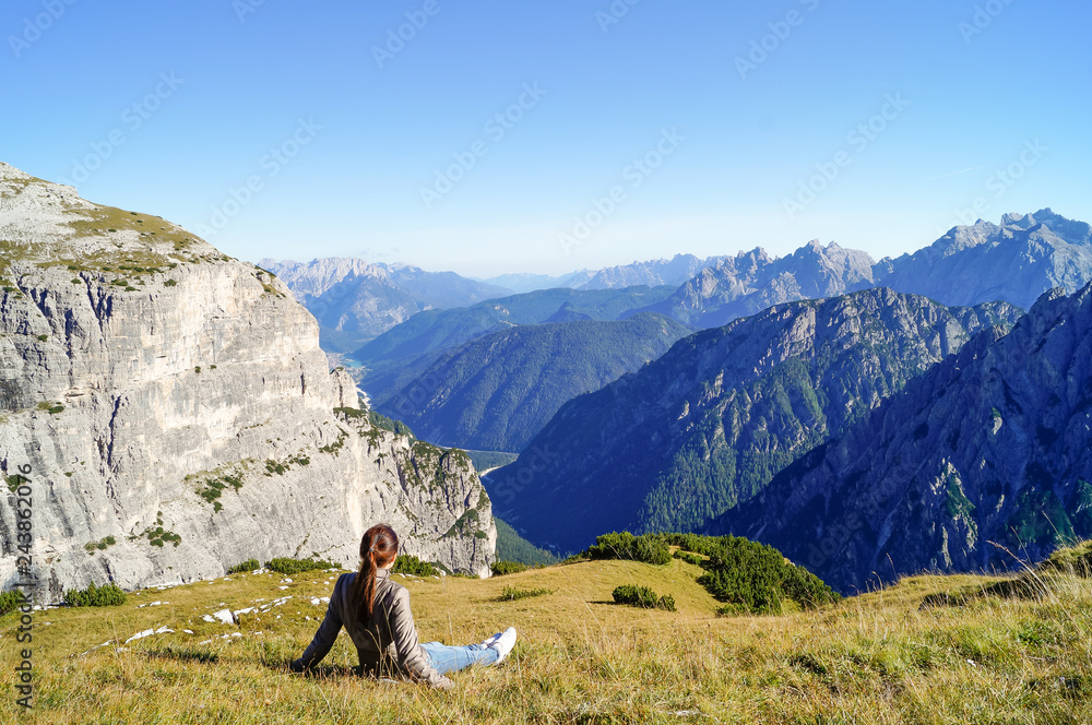 Naklejka premium girl sits on the grass and admires the beautiful mountain view in the Alps
