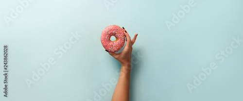 Female hand holding sweet donut over blue background. Top view, flat lay. Weight lost, sport, fitness, diet concept. Banner with copy space.