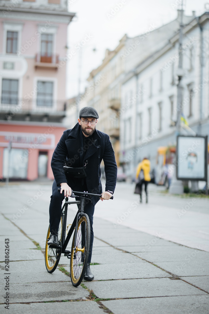 Bearded young businessman riding bicycle to work on urban street