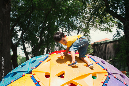 Asian kid boy having fun to play on children"s climbing toy at school playground, back to school outdoor activity.