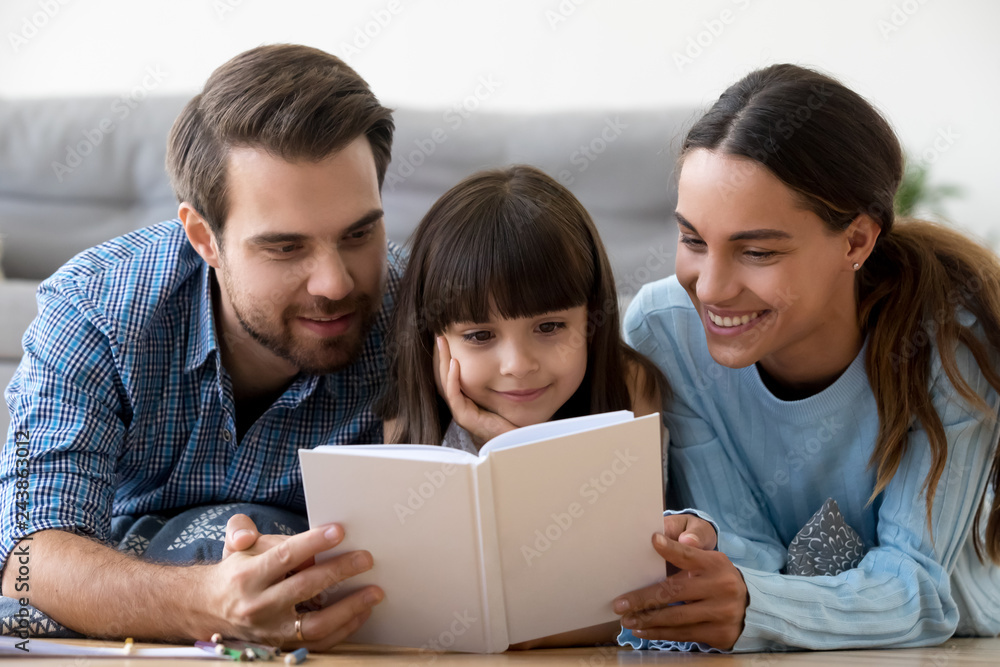 Happy mom and dad with little cute daughter holding reading book, smiling mother father and kid girl having fun playing at home spending time together, friendly parents and child readers concept Happy mom and dad with little cute daughter holding reading book, smiling mother father and kid girl having fun playing at home spending time together, friendly parents and child readers concept