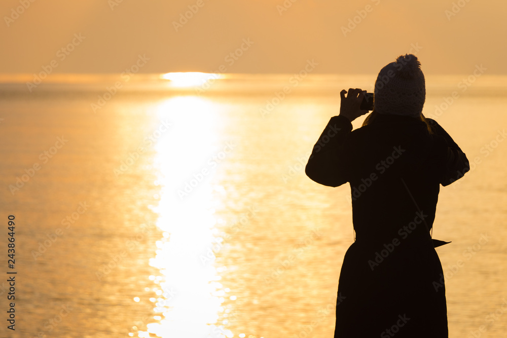 Silhouette.  Mature woman, takes photo of the sunset, using cell phone on the beach of the Black Sea. Autumn mood.