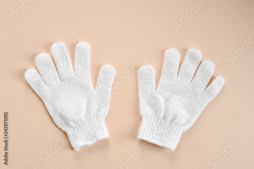 White exfoliating gloves. Polyacrylate gloves for use in the shower. Gloves tone, cleanse, massage the skin. Beige background. Close-up. View from above.