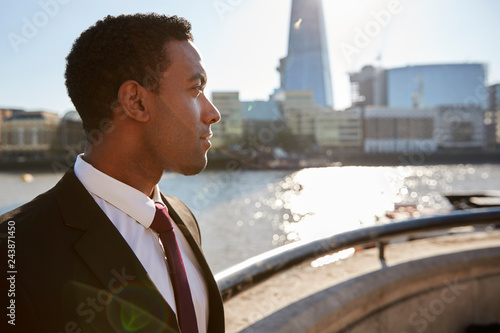 Young black businessman wearing shirt and tie standing by the River Thames, London, looking away, backlit © Monkey Business
