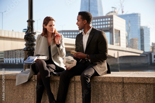 Photos Two millennial colleagues take a break sitting on the embankment eating near Lon
