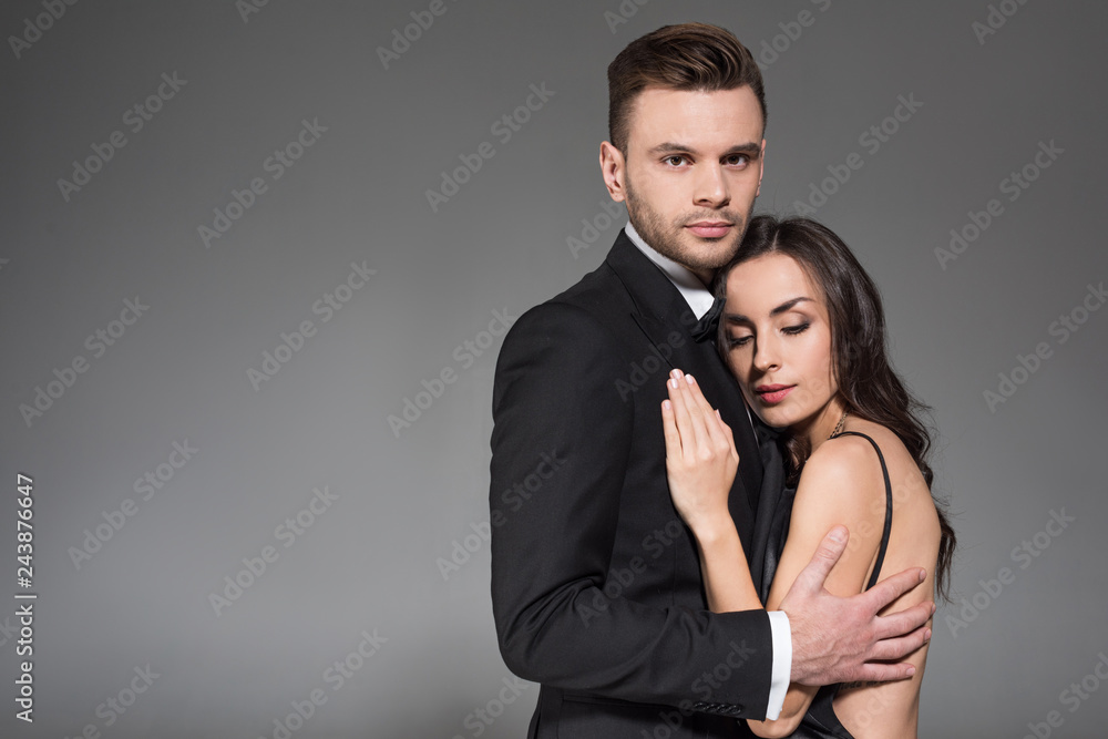beautiful elegant couple in black clothes hugging together isolated on grey beautiful elegant couple in black clothes hugging together isolated on grey