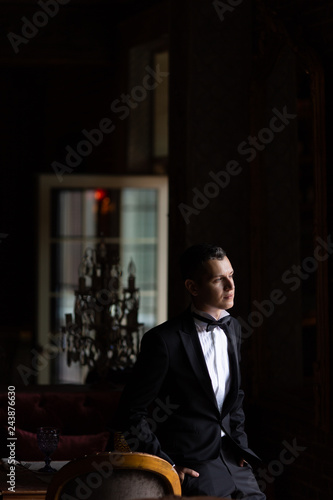 Pictures of elegant young man in bow tie sitting with hands in pockets, looking away from the camera