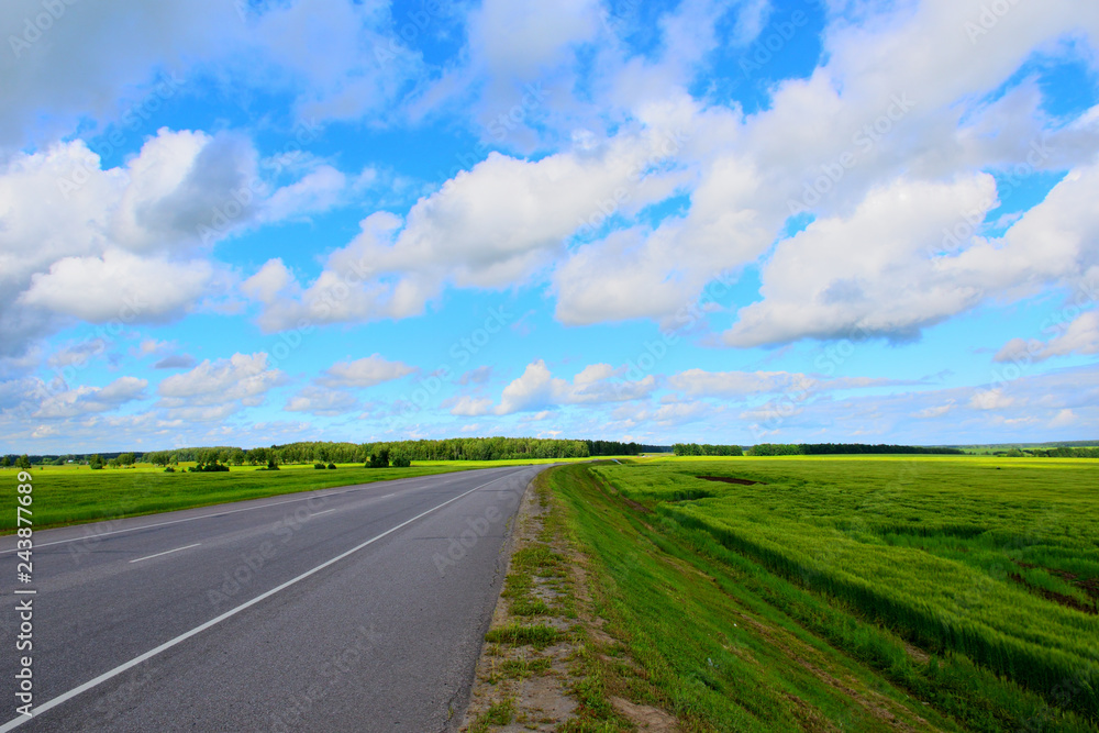 The road between green meadows on a background of bright blue sky