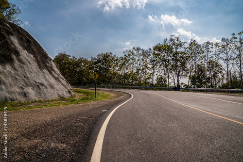 Road in the mountains. Empty asphalt road through the green Thailand hills and clouds on blue sky in summer day
