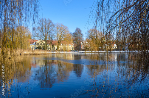 You see a wintry scene in Berlin, Germany, district Lichtenrade, with a village pond in the foreground and a small manor in the background. photo