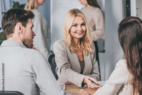 smiling mature businesswoman looking at young colleagues while working together in office