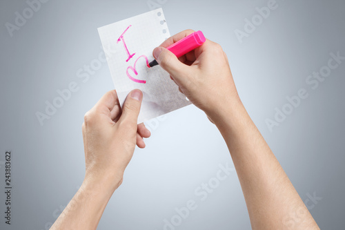 Hands writing a love note using a pink marker on gray background