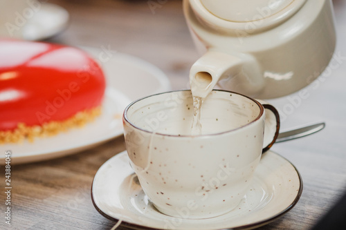 White ceramic teapot and cup on the table. Water is poured from the kettle. Against the background of reddish with icing.