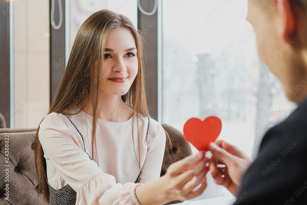 A girl gives or receives a valentine in the form of a red heart from a man in a cafe. A girl gives or receives a valentine in the form of a red heart from a man in a cafe.
