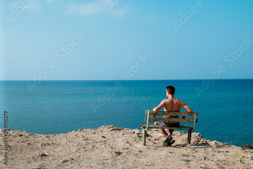 Rear view portrait of white man sitting relaxed on a bench and looking at the sea, man on a holiday. Cyprus