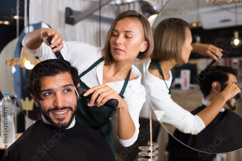 woman hairdresser shaving hair of smiling man