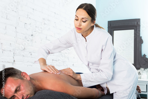 Fotografia Professional masseuse performing back massage to male client in spa center