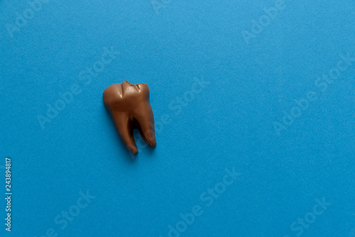 Obraz na plátně Bitten tooth from chocolate on blue paper background