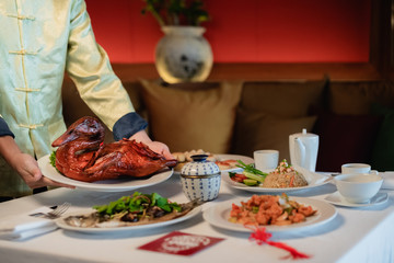 Concept picture for Chinese new year table set up and Chinese dishes. Men and Women are serving tea and crispy duck.