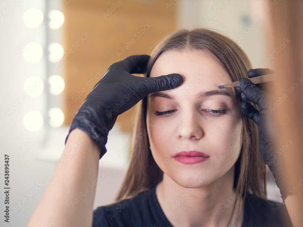 Fototapeta premium Master makeup corrects, and gives shape to pull out with forceps previously painted with henna eyebrows in a beauty salon. Professional care for face.